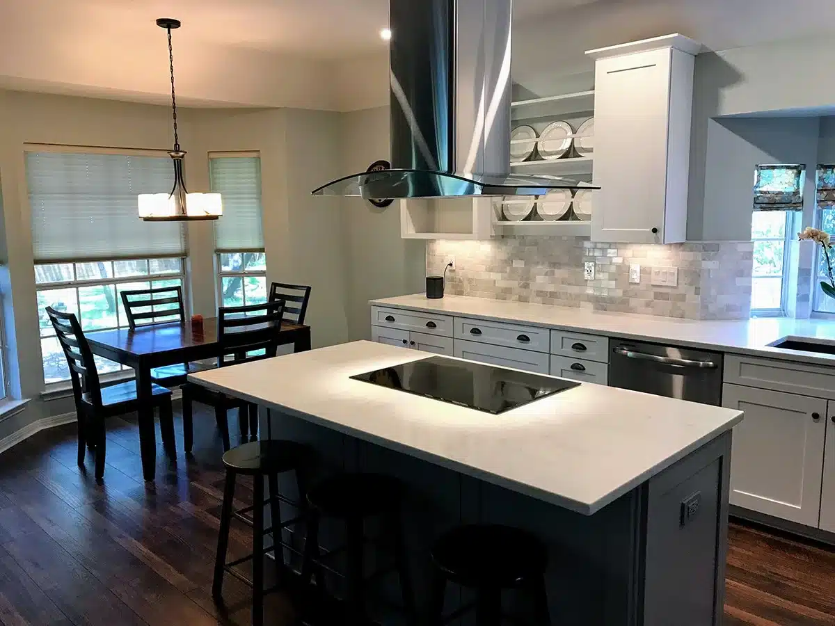 Kitchen island with a white countertop, black cooktop, and glass and stainless range hood beside a breakfast nook