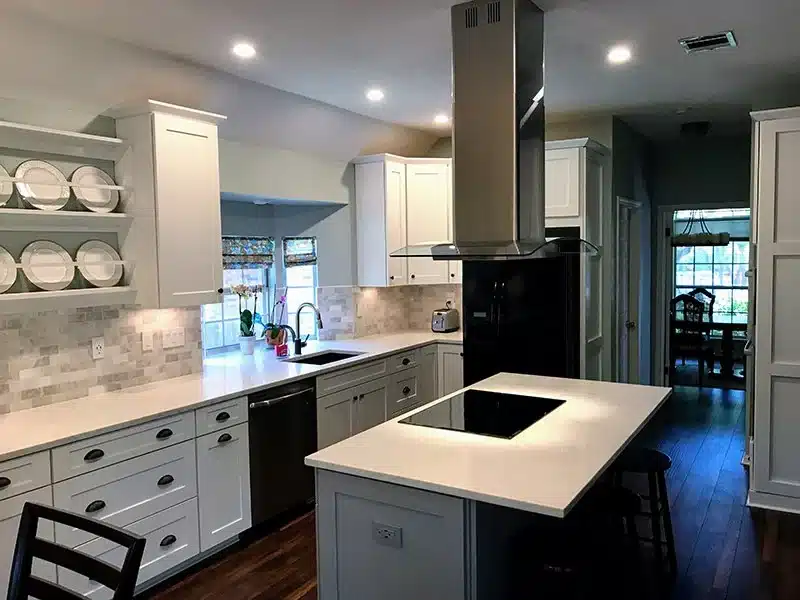White Shaker cabinets with a gray stone tile backsplash, an open plate rack, and an island cooktop under a stainless range hood
